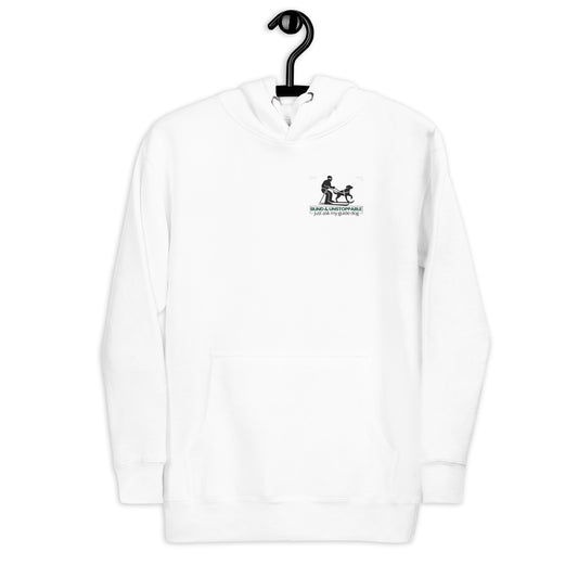 A bold, centered design features a black silhouette of a skier being guided by a harnessed dog, both in forward motion. Below the image, the phrase “BLIND &amp; UNSTOPPABLE – just ask my guide dog” appears in a mix of bold green sans-serif and regular black text. Framing lines and dotted corner accents convey momentum, partnership, and quiet determination.
