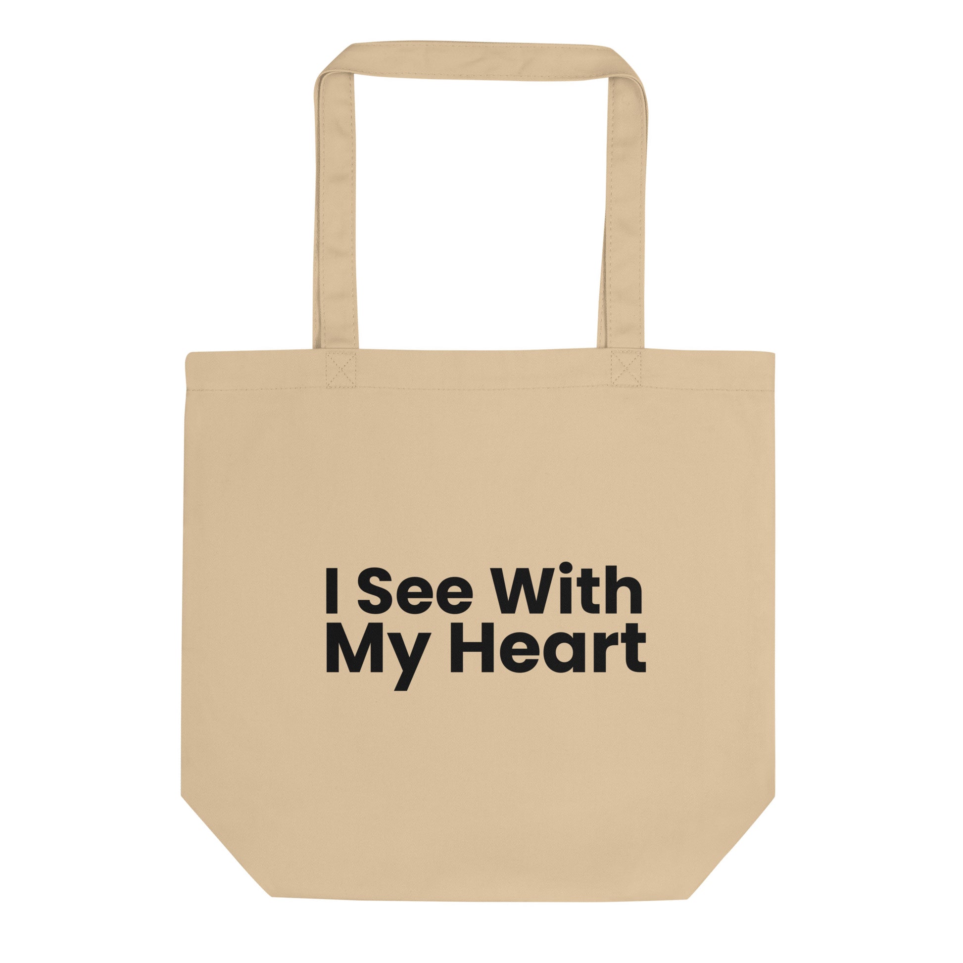 A tan-colored tote bag is displayed against a white background. The phrase "I See With My Heart" is printed in a bold, black, sans-serif font in the center of the bag. The text is stacked in three lines.