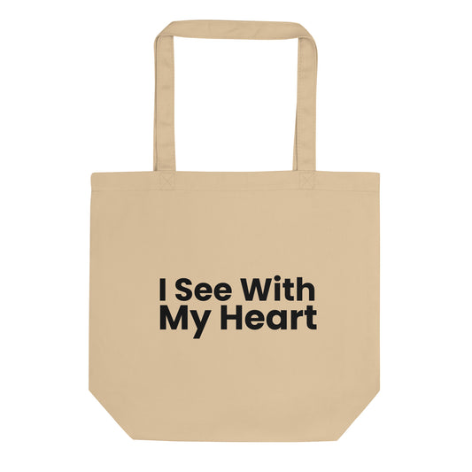 A tan-colored tote bag is displayed against a white background. The phrase "I See With My Heart" is printed in a bold, black, sans-serif font in the center of the bag. The text is stacked in three lines.
