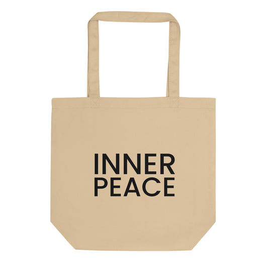 A light beige tote bag with the phrase "INNER PEACE" printed on the front in a bold, black, sans-serif font. The text is in all caps and stacked on two lines. The slogan represents a state of mental and spiritual calm, encouraging a feeling of contentment and serenity that comes from within.